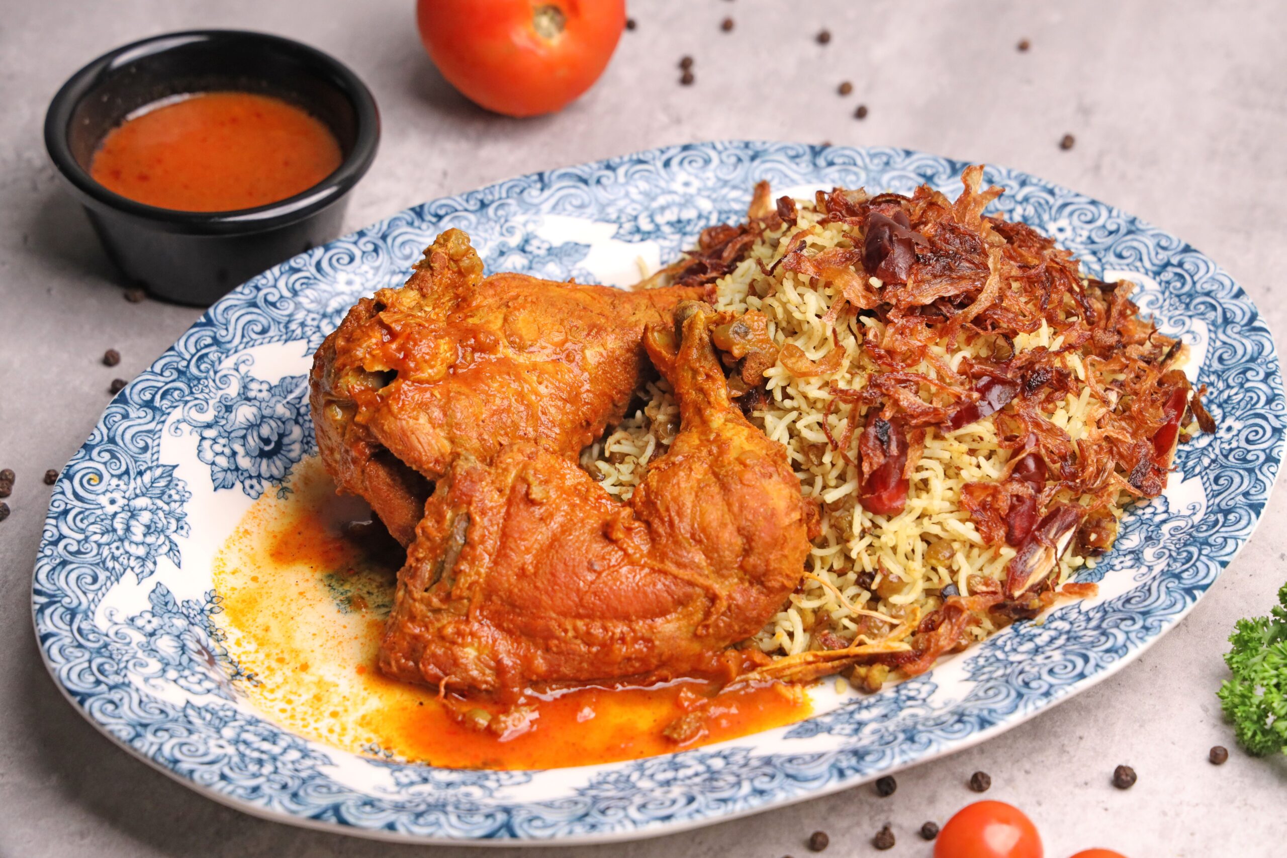 Close-up of flavorful fried chicken served with spiced rice and sauce on a ceramic plate.